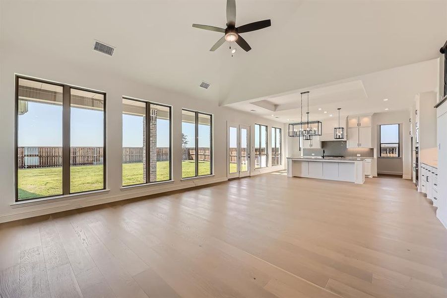 Living room with ceiling fan with notable chandelier, plenty of natural light, a raised ceiling, and light wood-type flooring