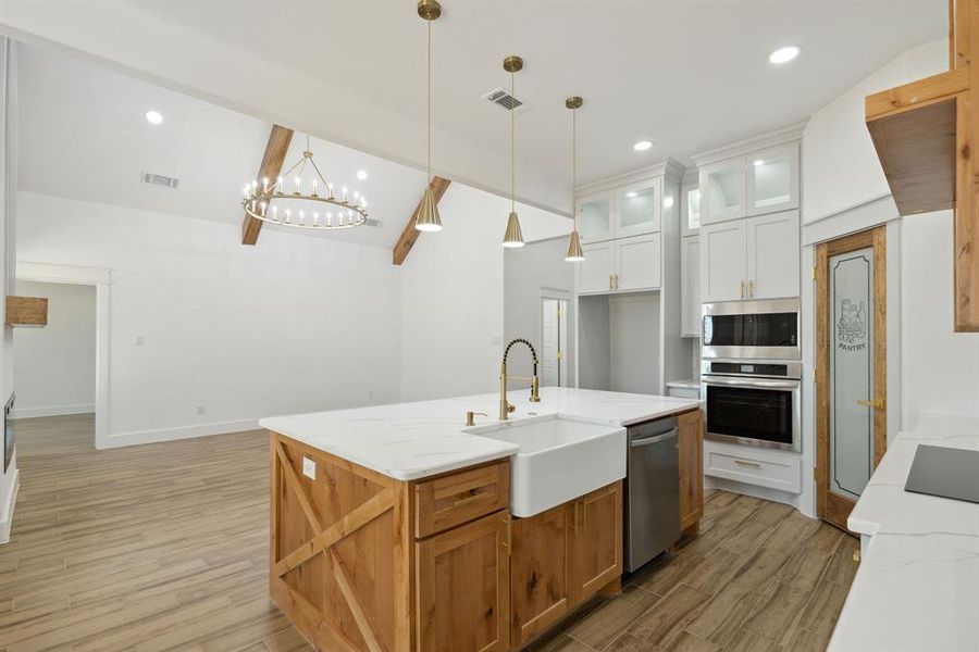 Kitchen with a center island with sink, appliances with stainless steel finishes, white cabinetry, lofted ceiling with beams, and sink