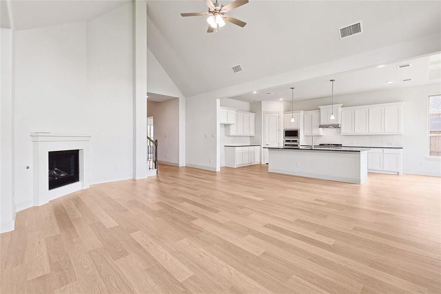 Unfurnished living room with high vaulted ceiling, ceiling fan, and light wood-type flooring