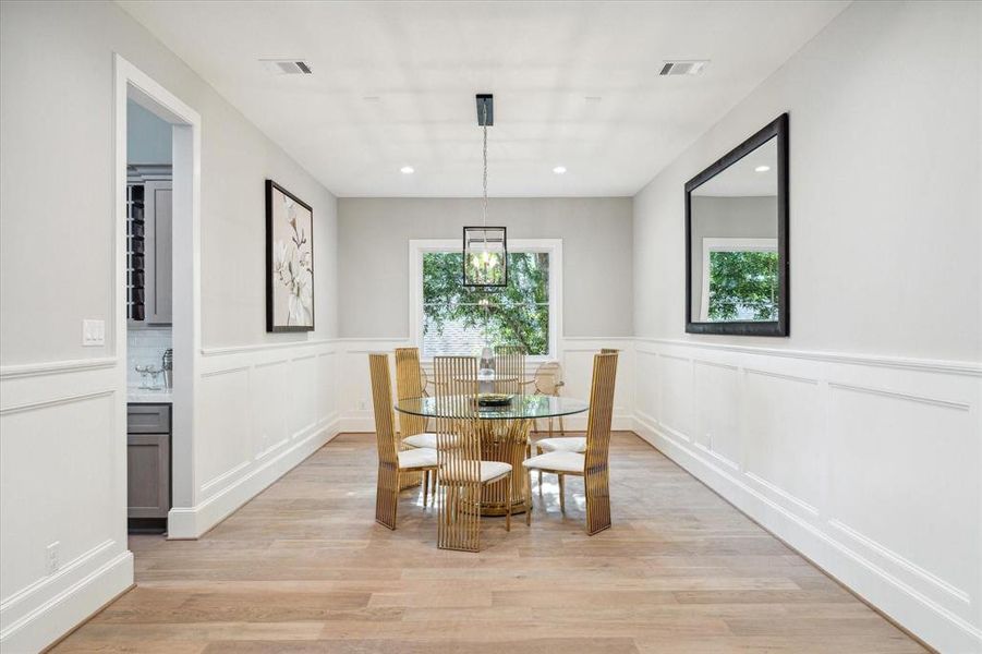 This is a bright and spacious dining area featuring elegant wainscoting, modern light fixtures, large windows that offer plenty of natural light. The room is finished with beautiful hardwood floors, providing a perfect space for a large dining furniture for entertaining and dining.
