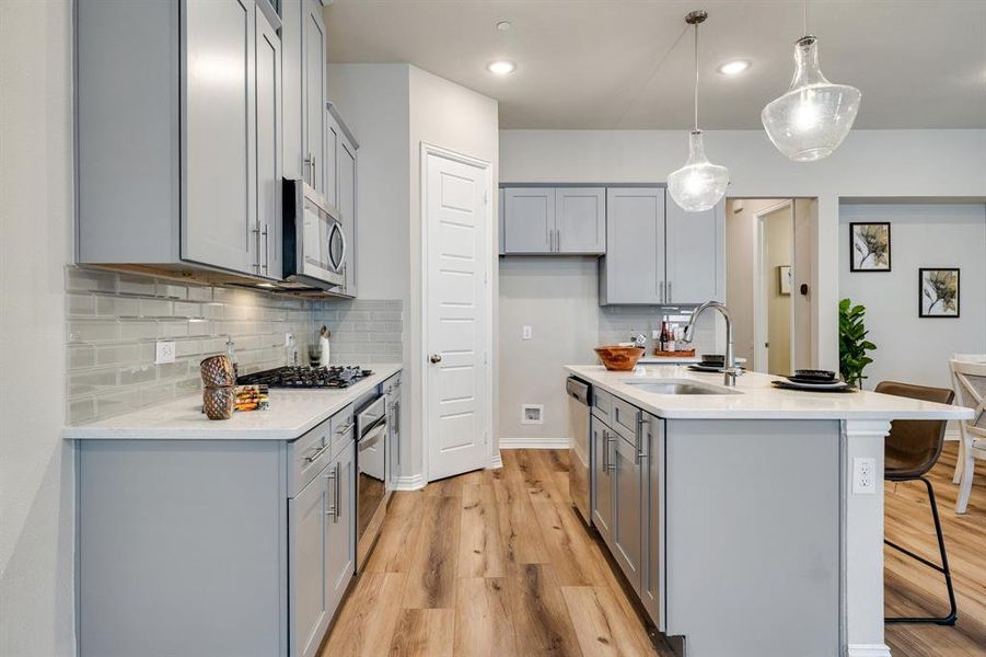 Kitchen featuring sink, hanging light fixtures, light hardwood / wood-style flooring, stainless steel appliances, and a center island with sink