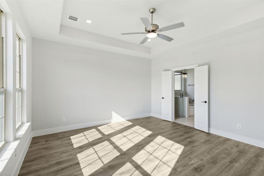 Unfurnished bedroom featuring hardwood / wood-style floors, ceiling fan, a tray ceiling, and connected bathroom