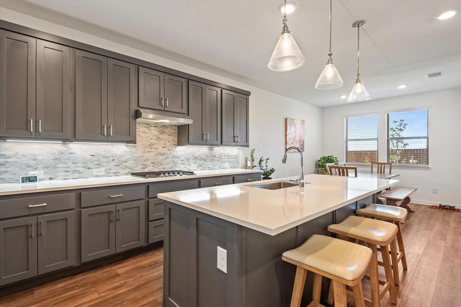 Kitchen featuring sink, decorative light fixtures, dark hardwood / wood-style floors, and a kitchen island with sink