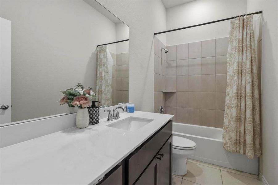 Full bathroom with tile floors, shower / bath combination with curtain, toilet, and vanity with extensive cabinet space