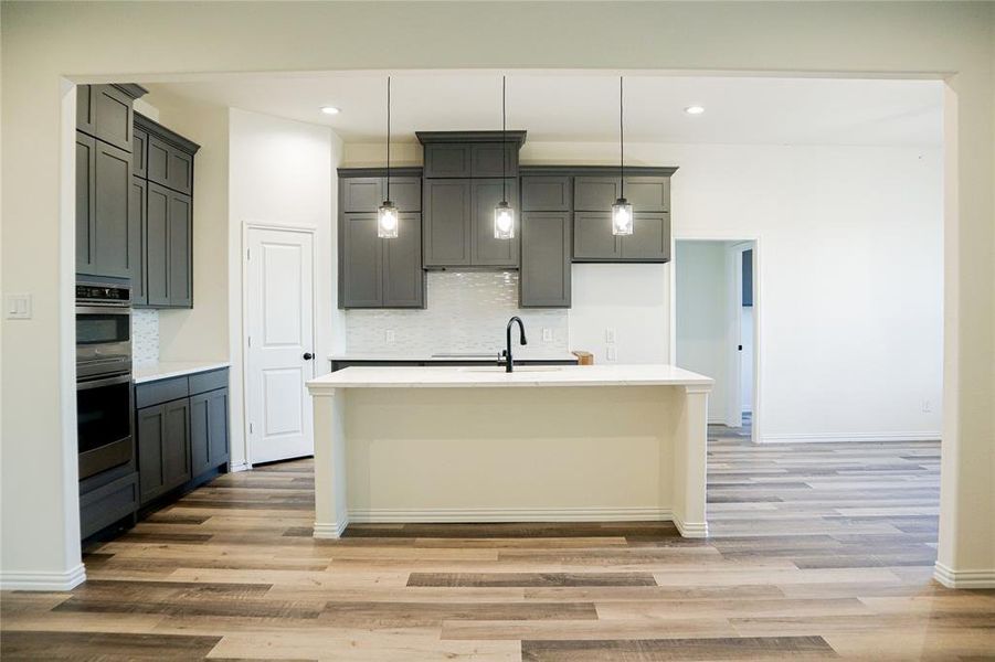 Kitchen featuring backsplash, light hardwood / wood-style flooring, hanging light fixtures, and gray cabinetry