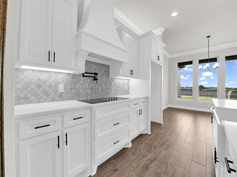 Kitchen featuring black electric stovetop, decorative light fixtures, custom range hood, backsplash, and white cabinets