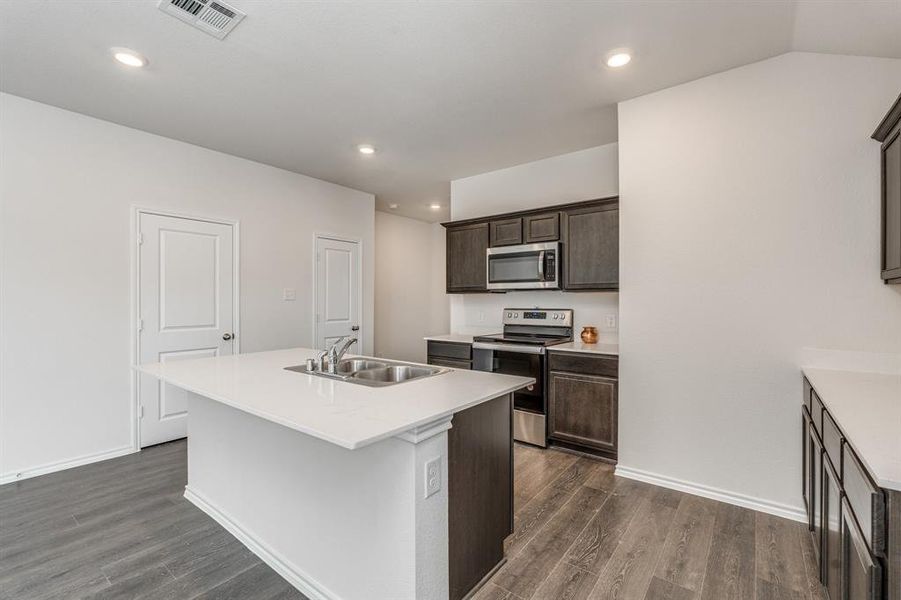 Kitchen with appliances with stainless steel finishes, dark hardwood / wood-style floors, dark brown cabinetry, a kitchen island with sink, and sink