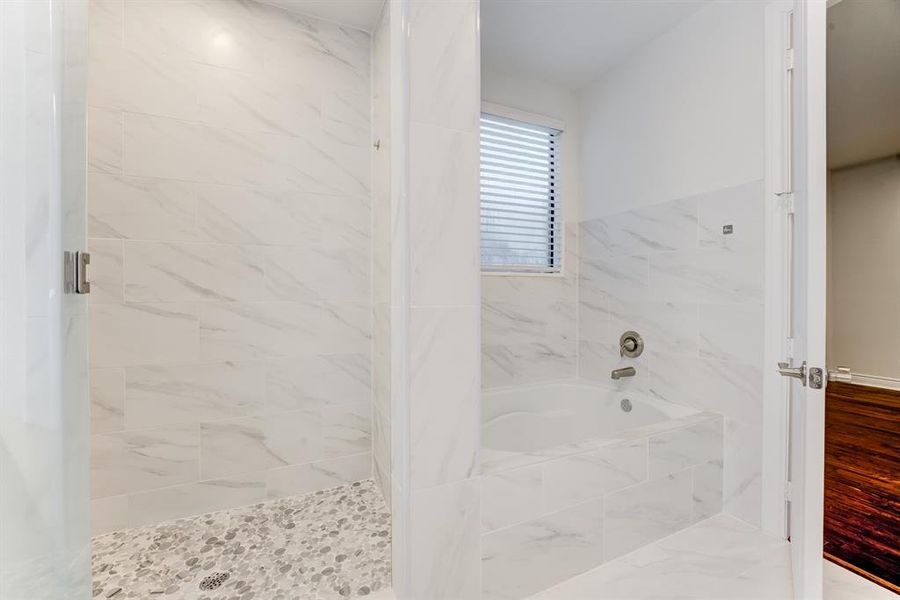 Primary en-suite features a glass-enclosed shower with a sleek white finish on the walls, a pebbled floor design in the shower area, and a separate soaking tub.