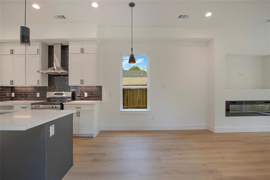 Kitchen with hanging light fixtures, wall chimney exhaust hood, stainless steel range oven, and white cabinetry