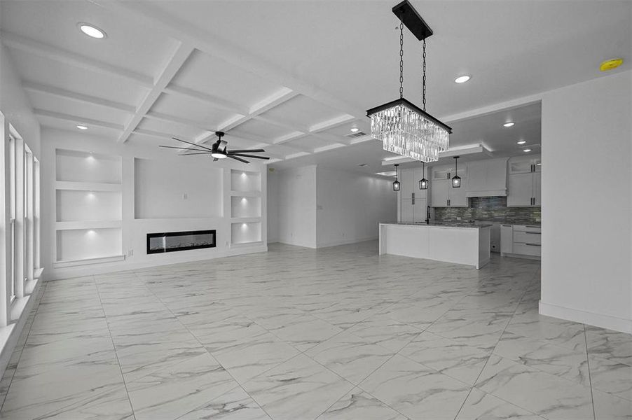 Unfurnished living room featuring light tile patterned flooring, ceiling fan with notable chandelier, beamed ceiling, and coffered ceiling