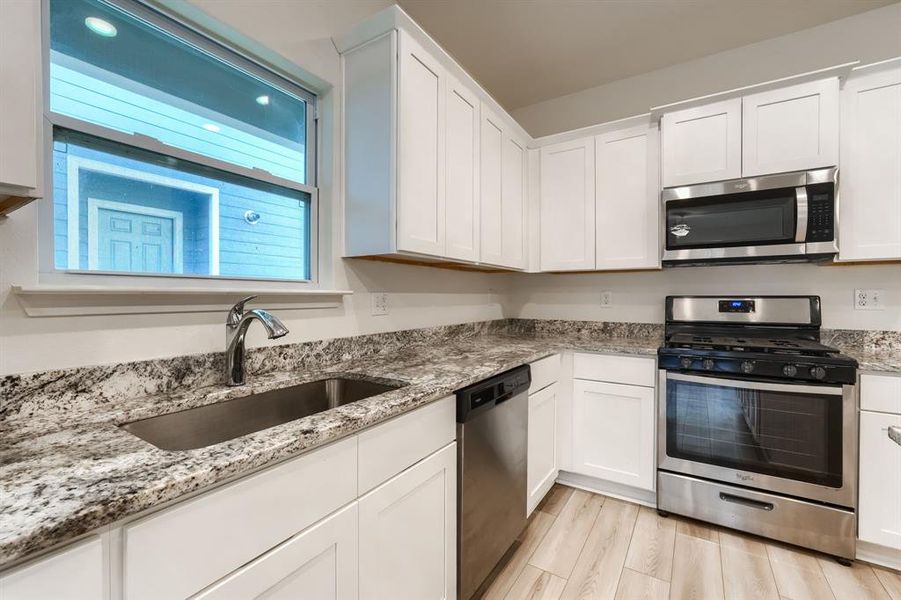 Kitchen with sink, appliances with stainless steel finishes, white cabinetry, and light hardwood / wood-style floors