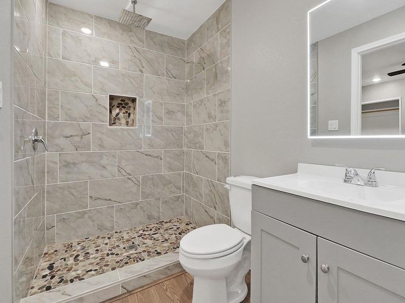 Bathroom featuring ceiling fan, vanity, tiled shower, hardwood / wood-style flooring, and toilet