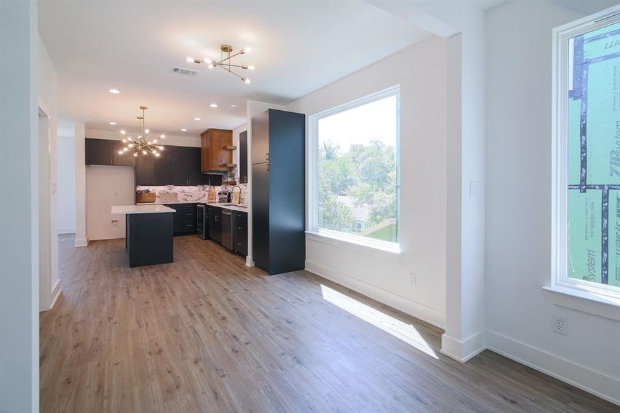 Kitchen featuring decorative backsplash, light hardwood / wood-style floors, a center island, decorative light fixtures, and a chandelier