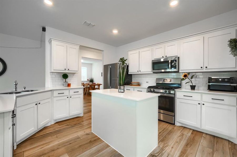 Kitchen featuring light hardwood / wood-style floors, sink, appliances with stainless steel finishes, a center island, and white cabinets