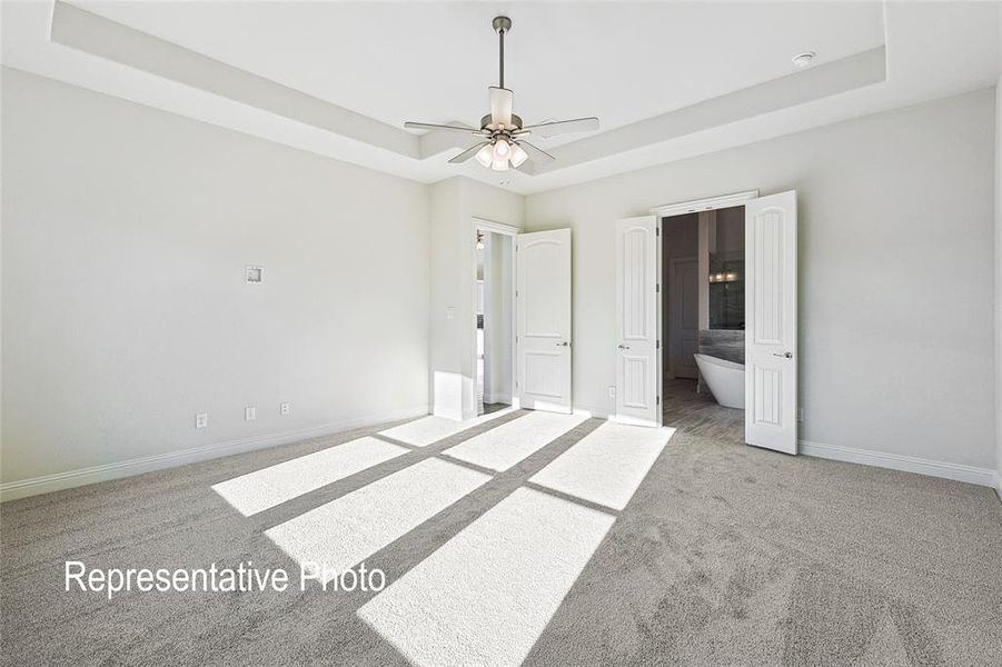 Unfurnished bedroom featuring ceiling fan, a tray ceiling, carpet floors, and ensuite bath