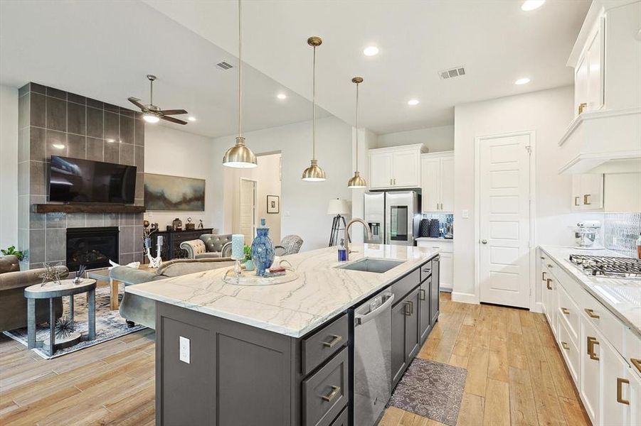 Kitchen with a kitchen island with sink, ceiling fan, white cabinets, and a tile fireplace