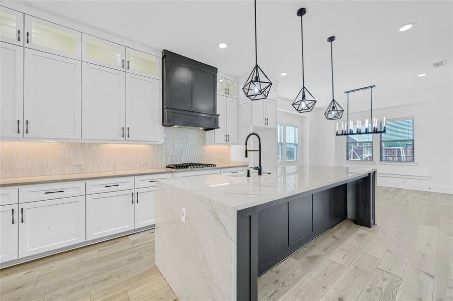 Kitchen featuring a waterfall kitchen island with sink, light LVP flooring, tasteful backsplash, and white cabinets