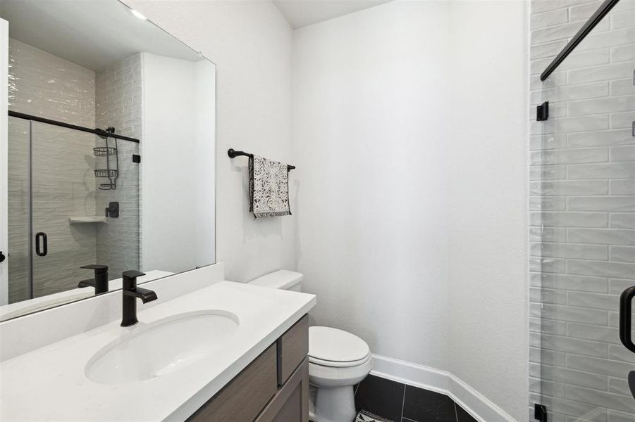 Secondary bathroom with matte black fixtures, a walk-in shower, and textured wall tiles.