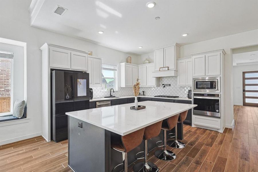 Kitchen with a breakfast bar area, dark hardwood / wood-style flooring, white cabinets, appliances with stainless steel finishes, and a center island