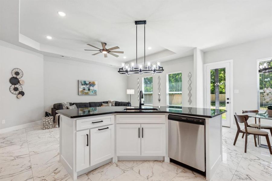 Kitchen with white cabinets, decorative light fixtures, sink, dishwasher, and a raised ceiling
