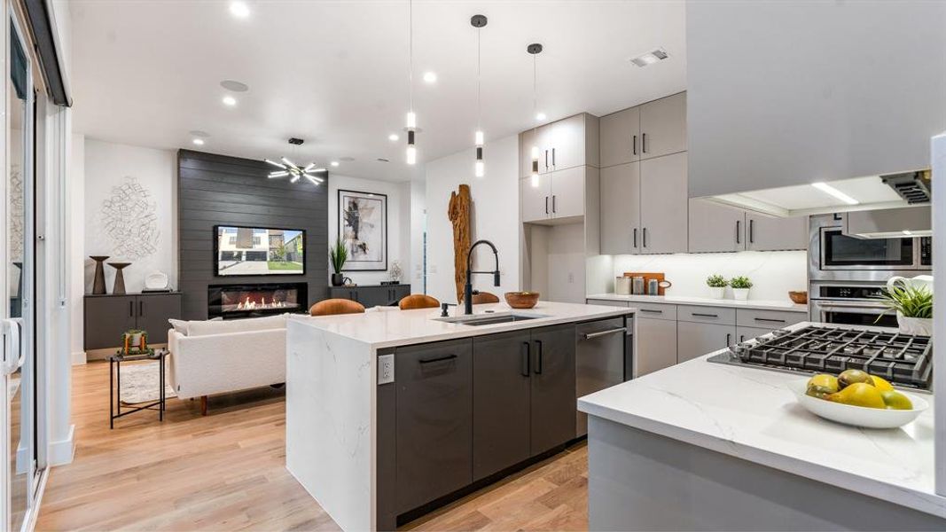 Kitchen with a fireplace, light wood-type flooring, appliances with stainless steel finishes, pendant lighting, and sink
