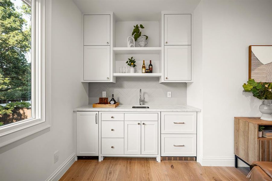 Bar with white cabinets, a wealth of natural light, light wood-type flooring, and sink