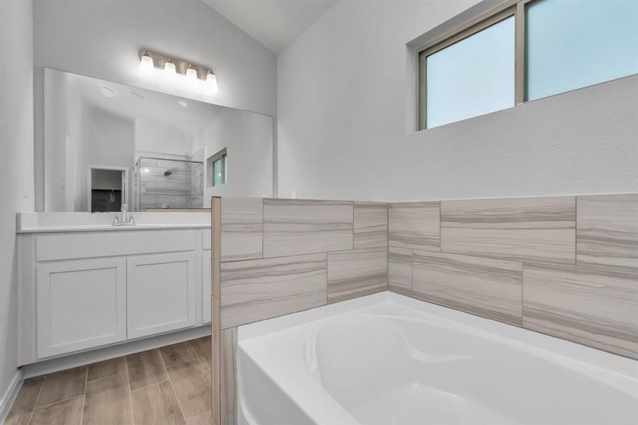 Indulge in the luxurious primary bathroom, featuring a spacious soaking tub and a glass-enclosed shower. The contemporary tile design adds a touch of elegance, creating a serene retreat where you can unwind after a long day. **This image is from another Saratoga Home - Wren floorplan.**