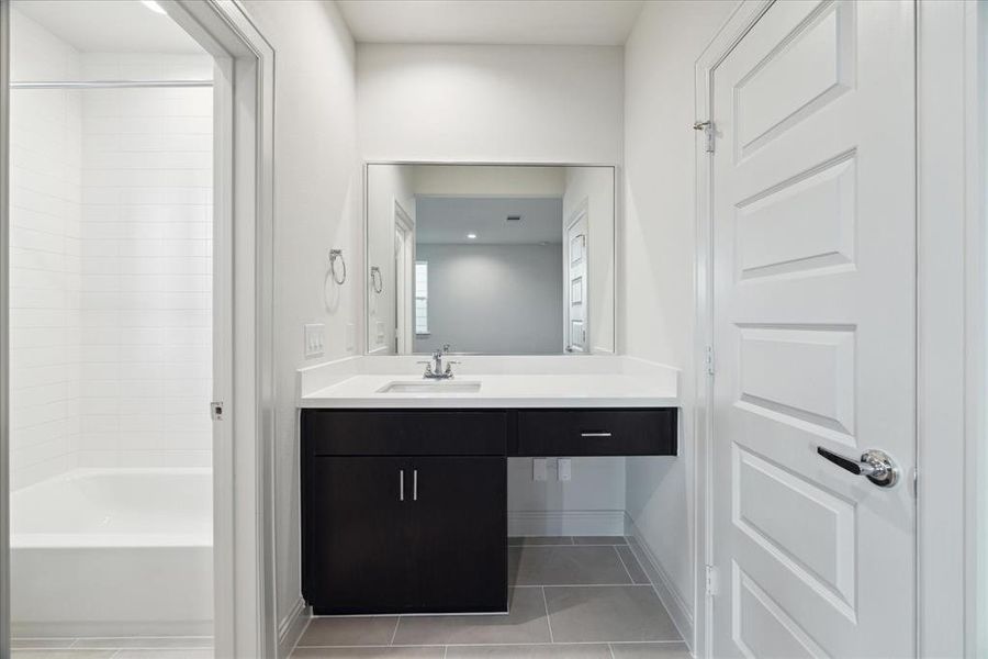 This modern first-floor ensuite bathroom offers a sleek design with a spacious vanity and plenty of counter space. The door on the left leads to a walk-in closet, while the galley layout provides easy access to the shower/tub combination located in a separate water closet for added privacy. Clean lines, bright lighting, and neutral tones create a functional and welcoming space, perfect for guests or daily use.