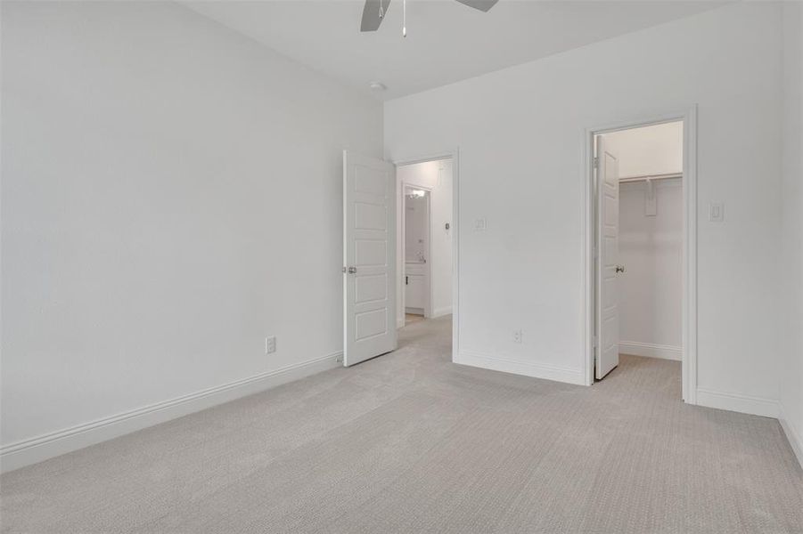 Unfurnished bedroom with light colored carpet, a walk in closet, and ceiling fan