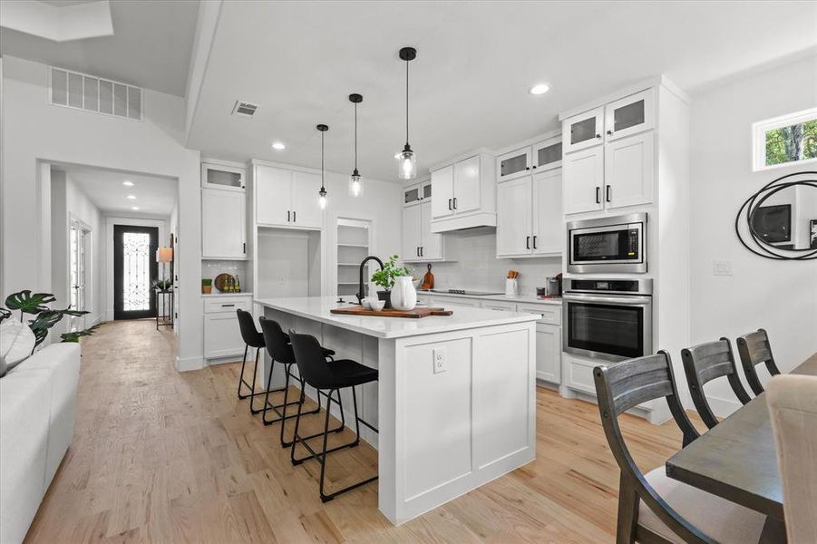 Kitchen featuring decorative light fixtures, light hardwood / wood-style floors, an island with sink, stainless steel appliances, and white cabinets