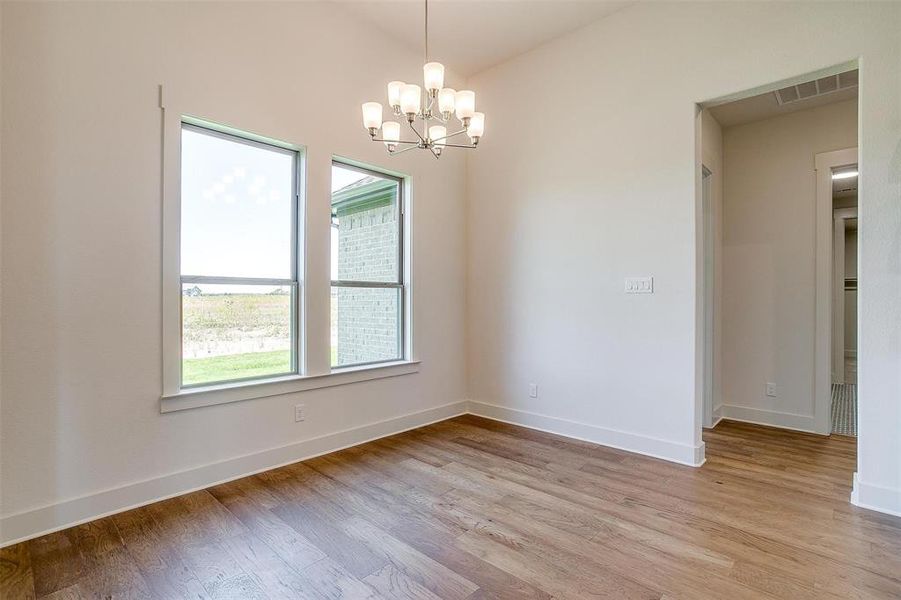 Empty room featuring a chandelier, a wealth of natural light, and wood-type flooring