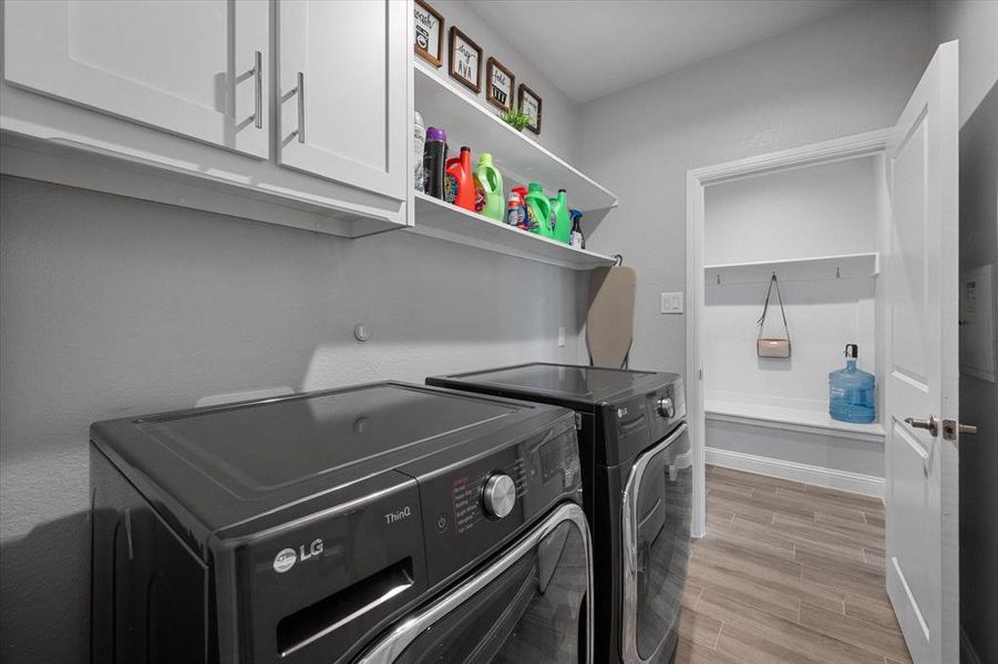 Clothes washing area featuring light wood-type flooring, washing machine and clothes dryer, and cabinets