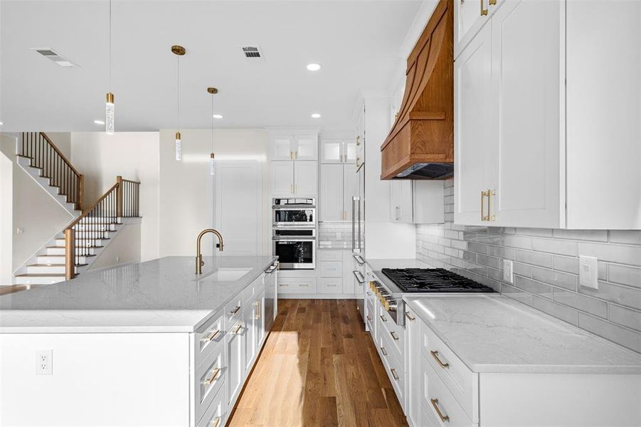 Kitchen with a kitchen island with sink, decorative light fixtures, sink, appliances with stainless steel finishes, and white cabinetry