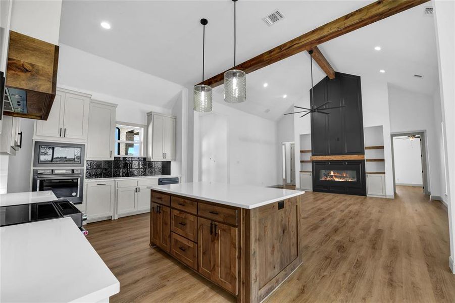 Kitchen featuring ceiling fan, light hardwood / wood-style flooring, high vaulted ceiling, a center island, and a fireplace