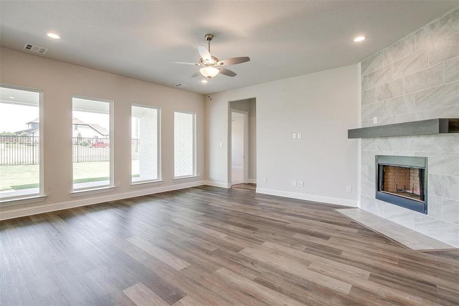 Unfurnished living room featuring ceiling fan, tile walls, a tiled fireplace, and hardwood / wood-style floors