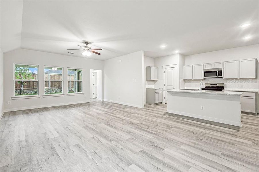 Kitchen with light wood-type flooring, ceiling fan, an island with sink, and stainless steel appliances