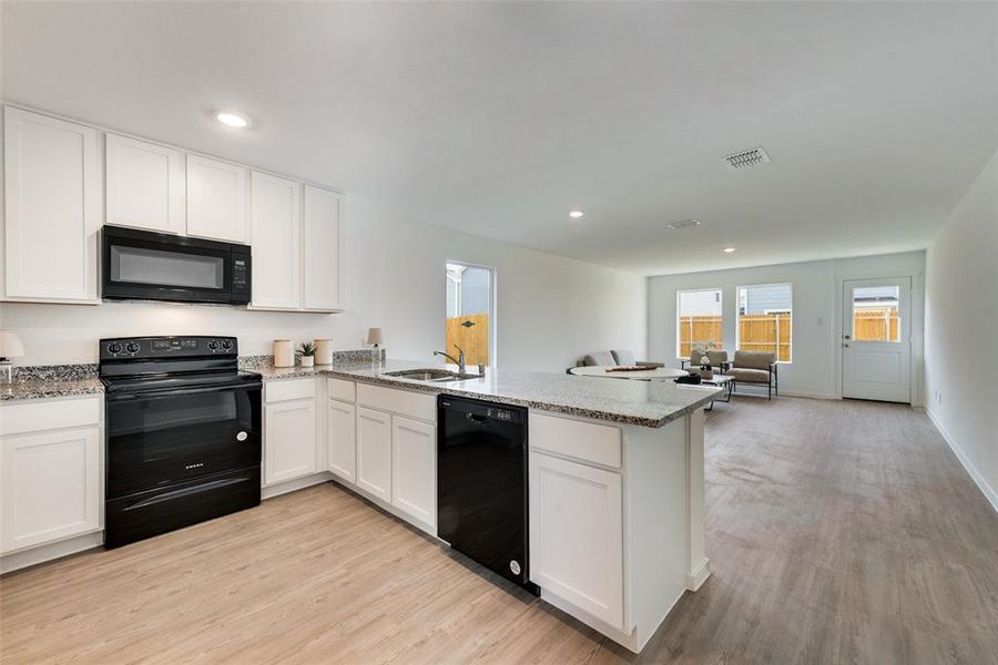 Kitchen featuring sink, kitchen peninsula, white cabinetry, black appliances, and light wood-type flooring