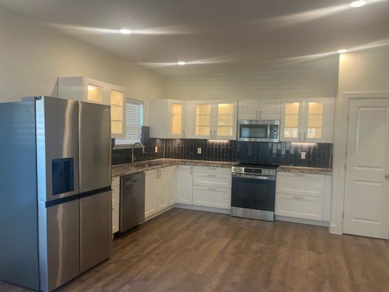 Kitchen with dark wood-type flooring, stainless steel appliances, white cabinets, and tasteful backsplash