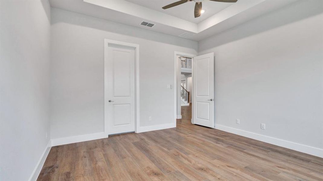 Unfurnished bedroom featuring ceiling fan, a tray ceiling, and light hardwood / wood-style flooring