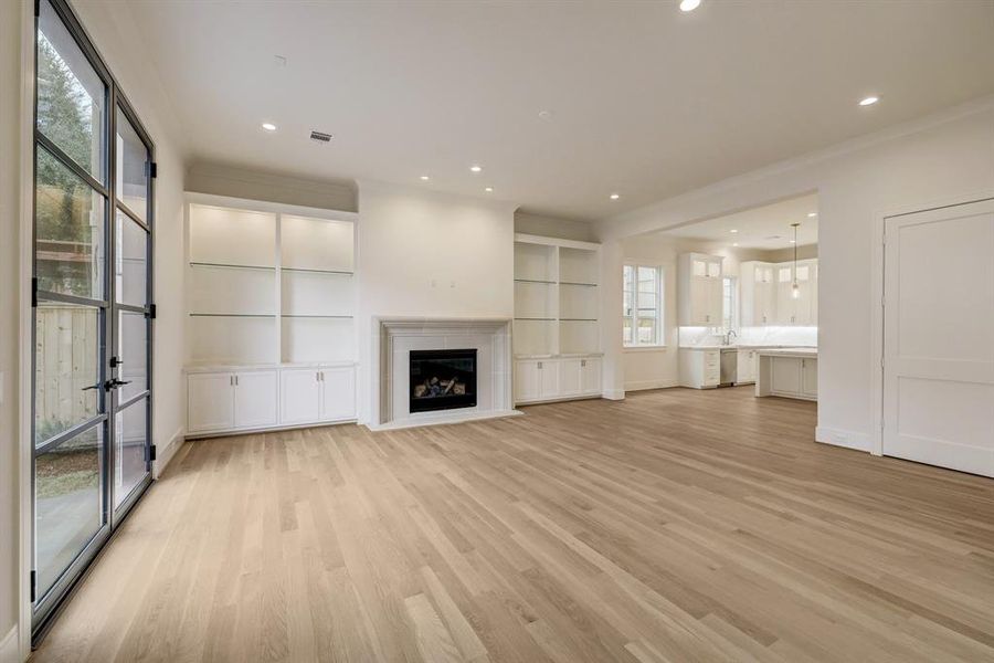 The living room features custom built-in cabinetry with glass shelves and marble countertops flanking the custom stone surround gas fireplace with logs.