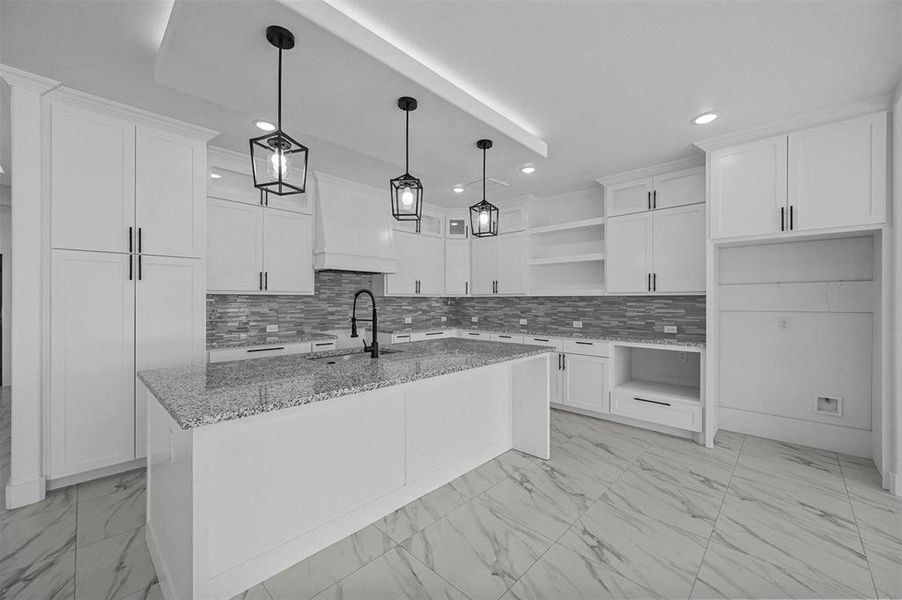 Kitchen featuring hanging light fixtures, sink, white cabinetry, and a kitchen island with sink