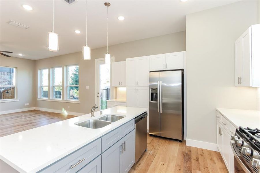 Kitchen with an island with sink, sink, white cabinetry, stainless steel appliances, and light wood-type flooring