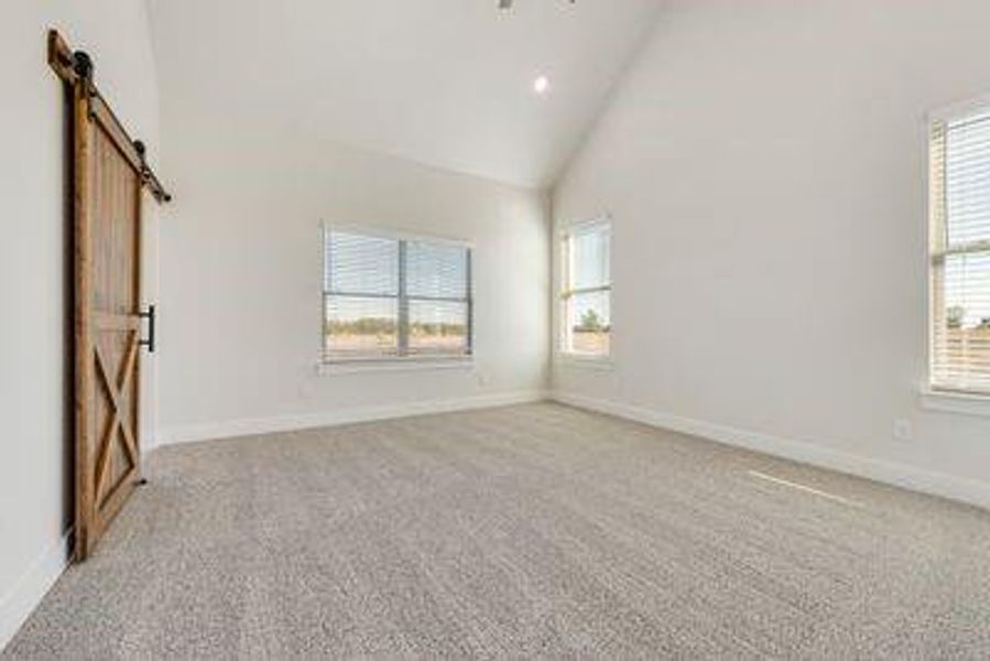 Empty room featuring a barn door, light carpet, and high vaulted ceiling