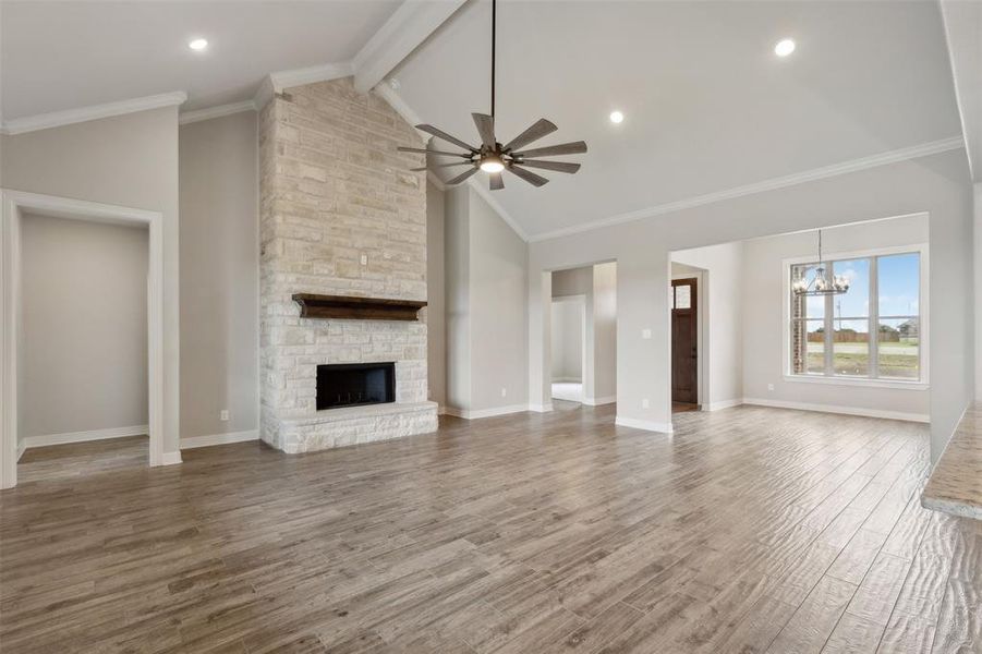 Unfurnished living room with beamed ceiling, hardwood / wood-style flooring, ceiling fan with notable chandelier, a stone fireplace, and crown molding