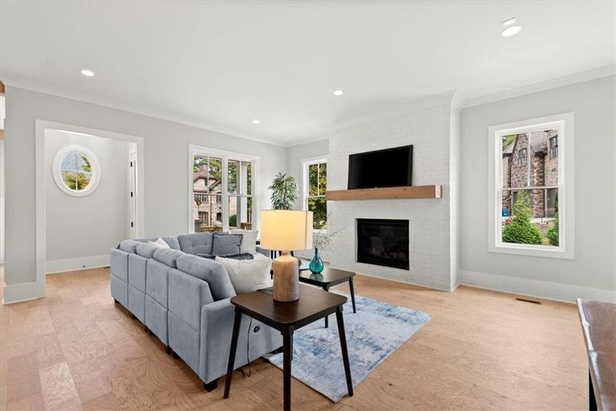 Living room featuring ornamental molding, a fireplace, light hardwood / wood-style flooring, and brick wall