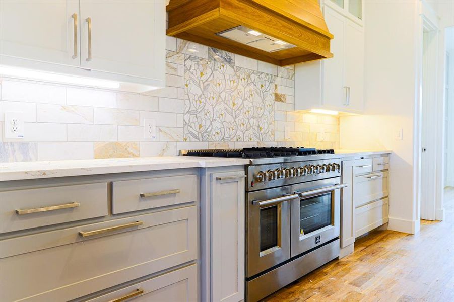 Kitchen featuring double oven range, decorative backsplash, custom exhaust hood, and light hardwood / wood-style floors