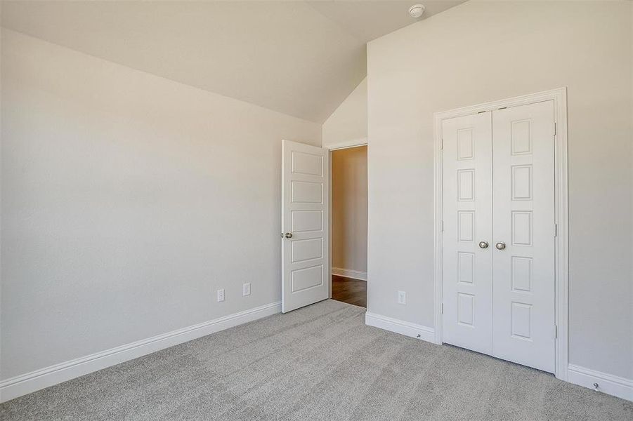 Unfurnished bedroom with vaulted ceiling, a closet, and light colored carpet