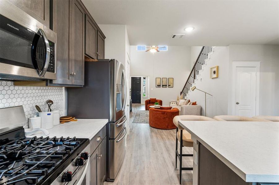 Kitchen with a kitchen breakfast bar, light hardwood / wood-style flooring, stainless steel appliances, backsplash, and dark brown cabinetry