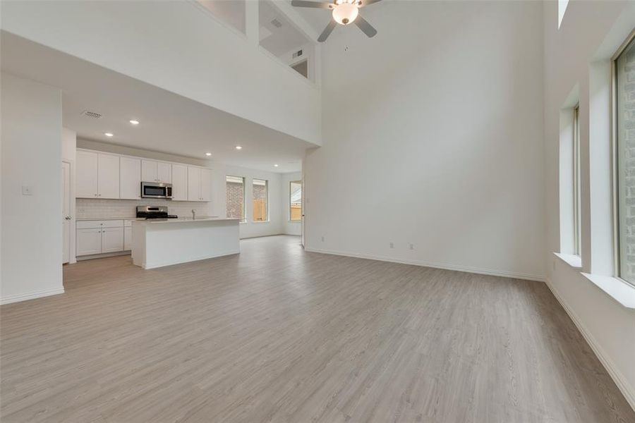 Unfurnished living room with a high ceiling, ceiling fan, and light hardwood / wood-style floors