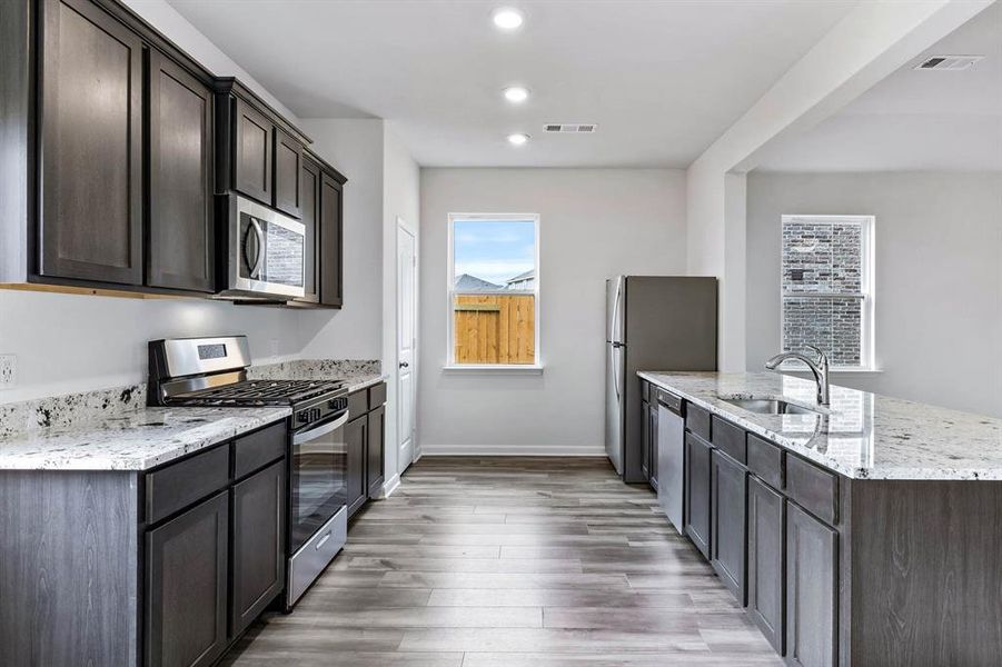 Kitchen with sink, light stone counters, dark brown cabinets, light hardwood / wood-style floors, and stainless steel appliances